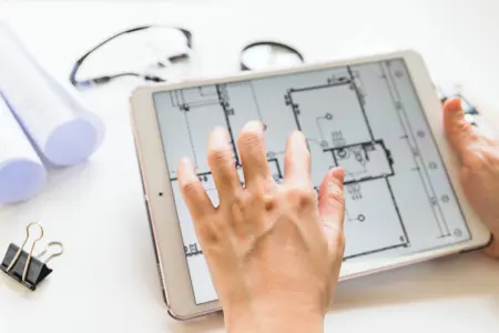 Architekt arbeitet an einem Hausprojekt mit einem Tablet und Bauplänen.